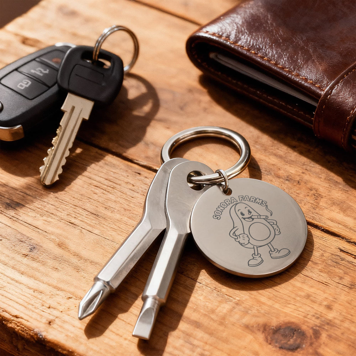 Silver logo screwdriver keychain beside keys and a wallet on a wooden surface