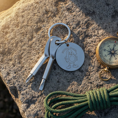 Silver screwdriver keychain with example company logo beside a compass outdoors