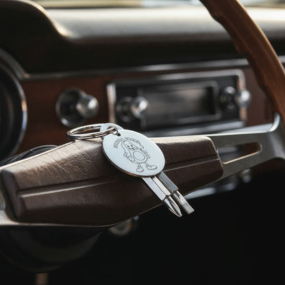 Silver engraved screwdriver keychain displayed on a vehicle steering wheel