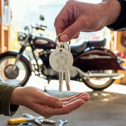 Silver logo screwdriver keychain held beside a motorcycle