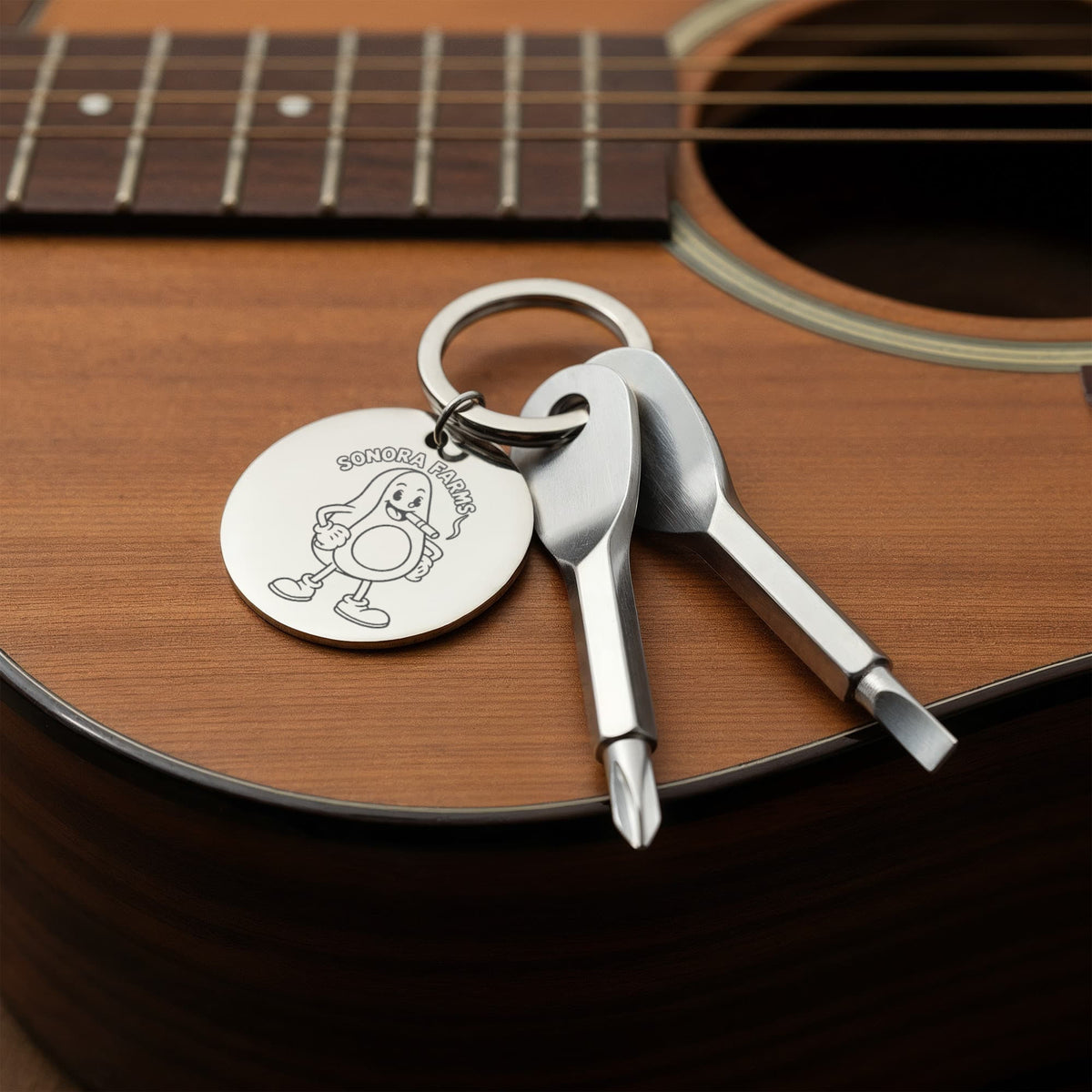 Silver screwdriver keychain with example logo resting on an acoustic guitar